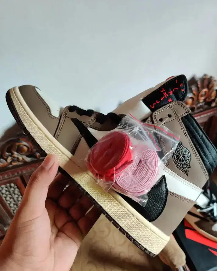 Travis Scott X Nike Air Jordan 1 High Cactus Jack Mocha sneaker with red and pink laces held in hand.