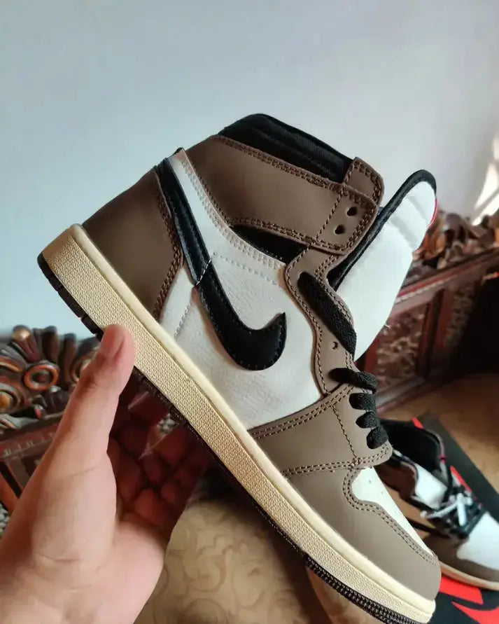 Hand holding Travis Scott X Nike Air Jordan 1 High Cactus Jack Mocha sneaker in brown and white.